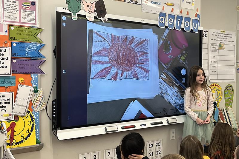 Pictured, first-grade student Amaya explains her own flag project to the​ class.